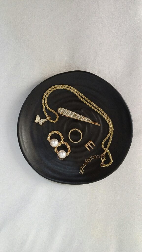 Stylish flat lay of gold jewelry pieces on a black plate, ideal for fashion or accessory themes.